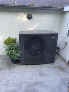 Udendørs varmepumpe ved siden af grøn plante.